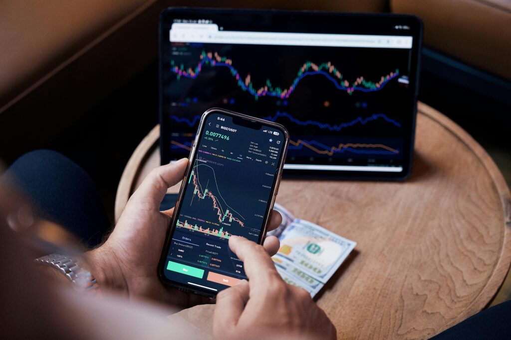 Close-up of a person trading stocks using a smartphone and a tablet.